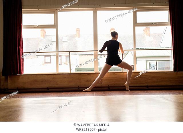 Ballerina stretching on barre while practicing ballet dance