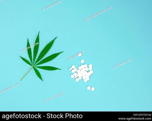 green leaf of hemp and white tablets on a blue background, concept of legalization of alternative treatment, top view