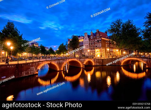 Night view of Amterdam cityscape with canal, bridge and medieval houses in the evening twilight illuminated. Amsterdam, Netherlands