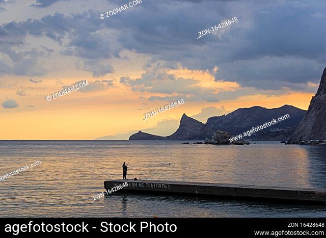 A lone fisherman on a breakwater in Sudak bay of Crimea at evening. Translation of phrase: