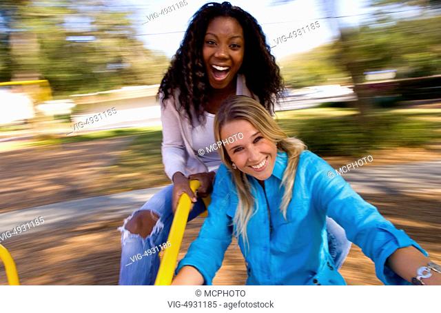 Attractive mixed ethnic women aged 20s having fun spinning on merry go round outdoors in park black african american and white blonde woman - 31/03/2020