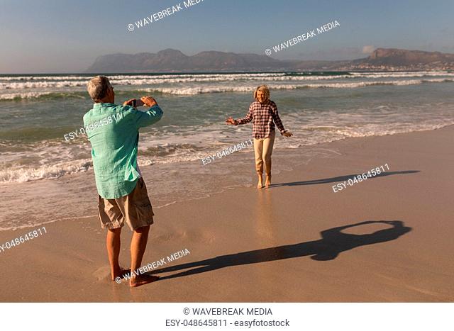 Senior man clicking photo of senior woman on the beach
