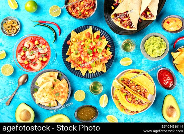 Mexican food, many dishes of the cuisine of Mexico, flat lay, shot from the top on a vibrant blue background. Nachos, tequila, guacamole etc