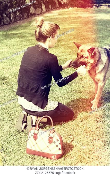 Vintage portrait with red stripe sun fade of a young woman in 20s playing stick with her German Shepherd dog at park. Inseparable relationship