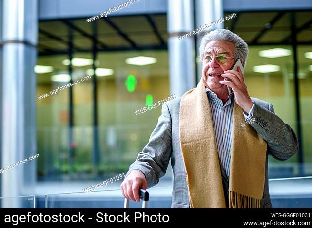 Senior businessman talking on mobile phone standing in front of glass wall
