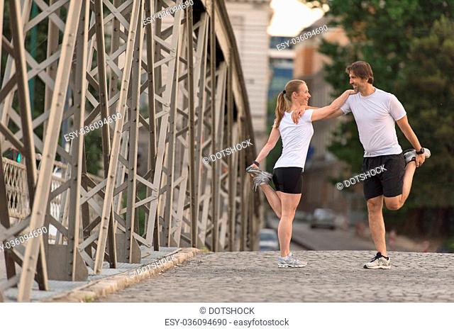 jogging couple warming up and stretching before morning running training workout in the city with sunrise in background