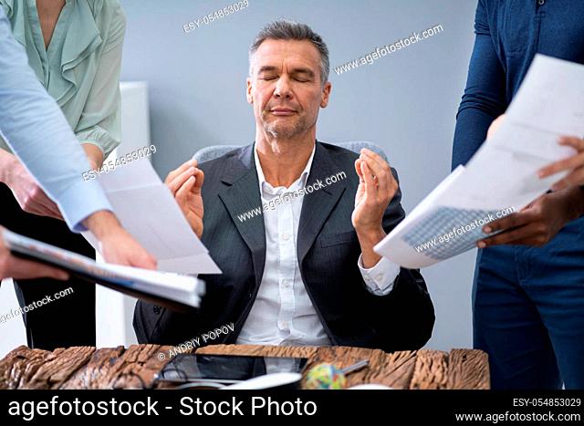Mature Businessman Meditating While Surrounded By His Executives