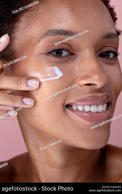 Close-up of smiling woman applying cream on face