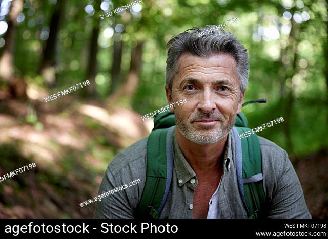 Smiling handsome male hiker with backpack in forest