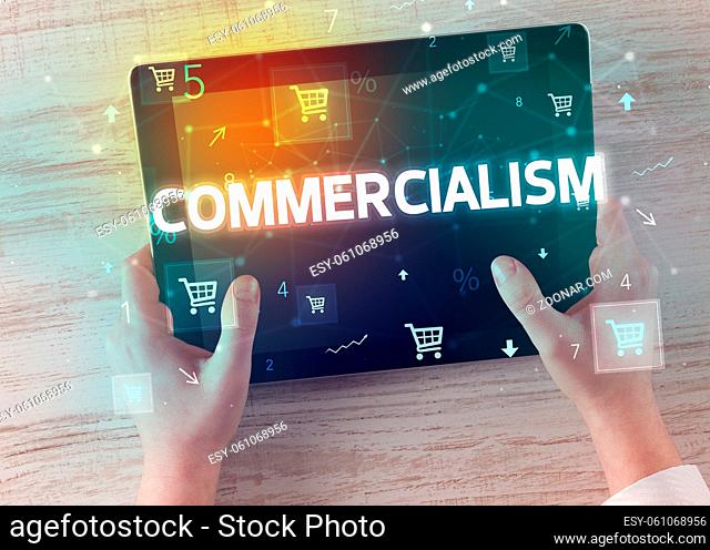 Close-up of a hand holding tablet with COMMERCIALISM inscription, online shopping concept