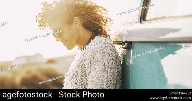 Side emotional portrait of serene and happy young woman looking down with a smile against a blue classic vehicle. Concept of travel lifestyle people