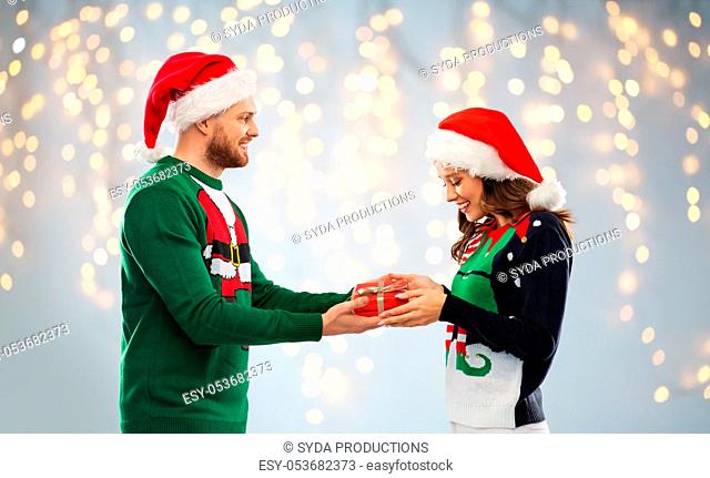 happy couple in ugly sweaters with christmas gift