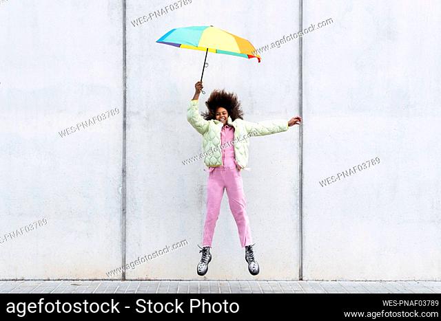 Happy girl jumping holding umbrella in front of white wall