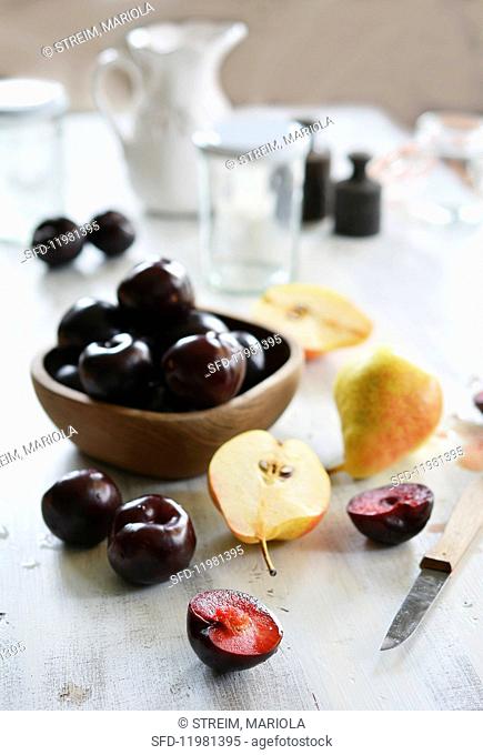Pears and plums on a white wooden table with empty jam jars and weights in the background