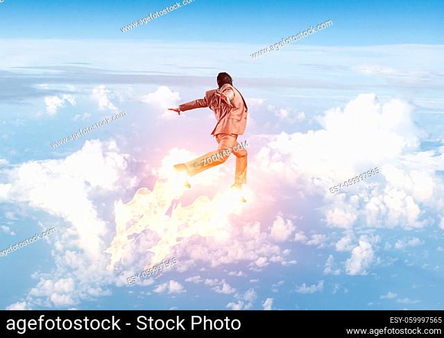 Expressive businessman in suit and aviator hat flying in blue sky as superhero. Business person as superman with jet flame above clouds