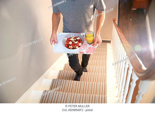 Young man carrying breakfast tray upstairs, neck down