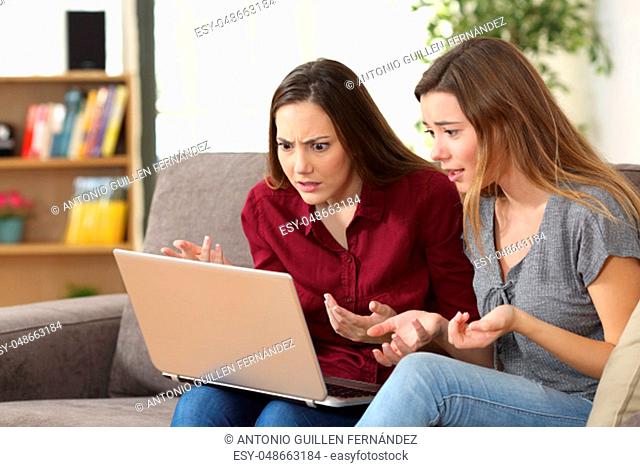 Two confused friends watching media content on line sitting on a sofa in the living room at home