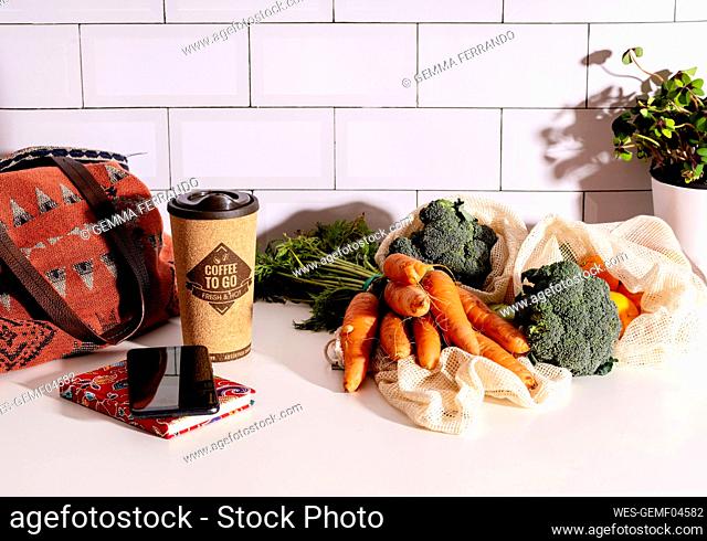Coffee to go in cork eco mug, smart phone and organic veggies in mesh reusable bags on kitchen counter