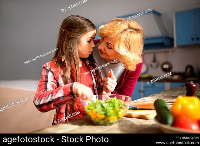 Granny and littlr girl in cozy kitchen. Preparing salad for lunch