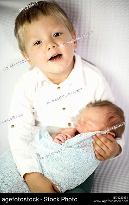 Three years old boy holding his newborn baby brother