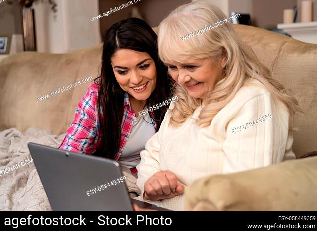 Beautiful Daughter Show Her Elderly Mother How To Use The Laptop Sitting On The Sofa In The Living Room