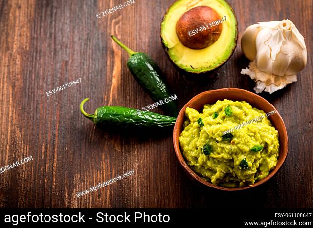 Guacamole with ingredients on wooden table