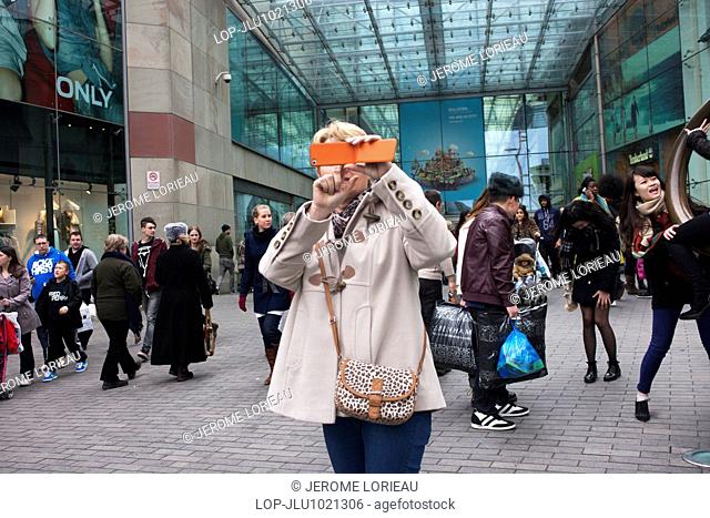England, West Midlands, Birmingham. A woman taking a photograph with her mobile phone outside the Bullring shopping centre