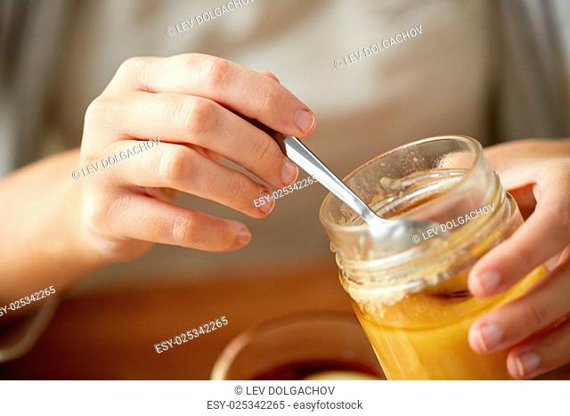 health, traditional medicine and ethnoscience concept - close up of woman hands with honey jar and spoon