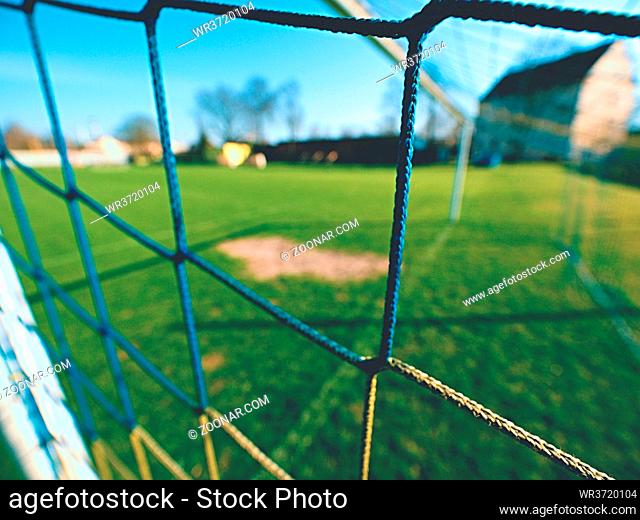 Detail of yellow blue crossed soccer nets, soccer football in goal net with grass on outdoor playground in the background