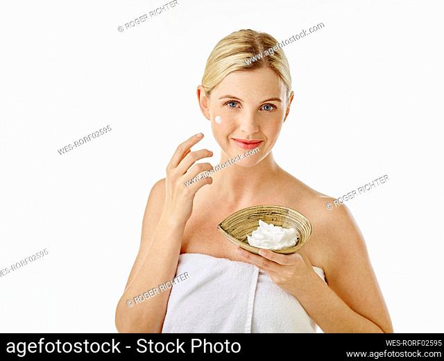 Woman holding face cream bowl while standing against white background