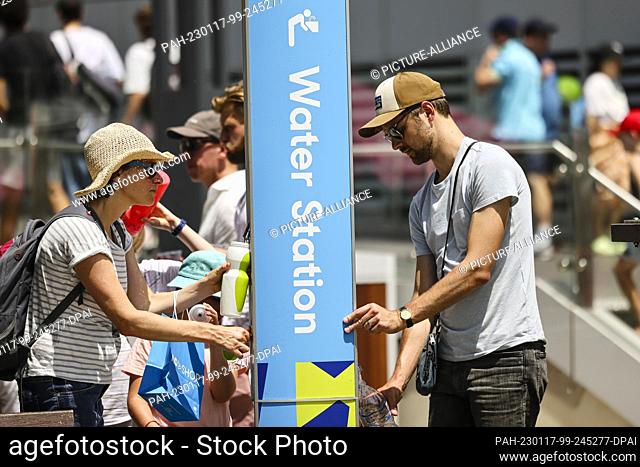17 January 2023, Australia, Melbourne: A man and a woman fill bottles with water. Due to extreme temperatures, matches at the Australian Open were paused on the...