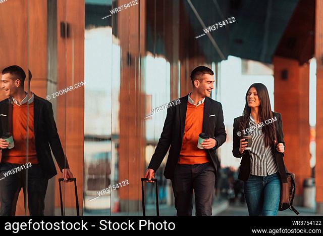 Businessman and businesswoman talking and holding luggage traveling on a business trip, carrying fresh coffee in their hands. Business concept