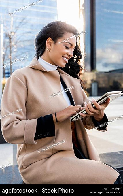 Smiling businesswoman in overcoat using laptop on seat