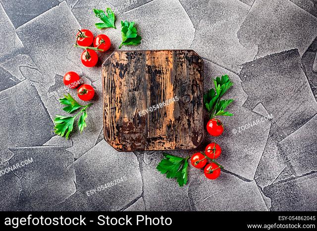 Fresh vegetables tomatoes and parsley around vintage cutting board on grey background, top view, place for text. Vegan food