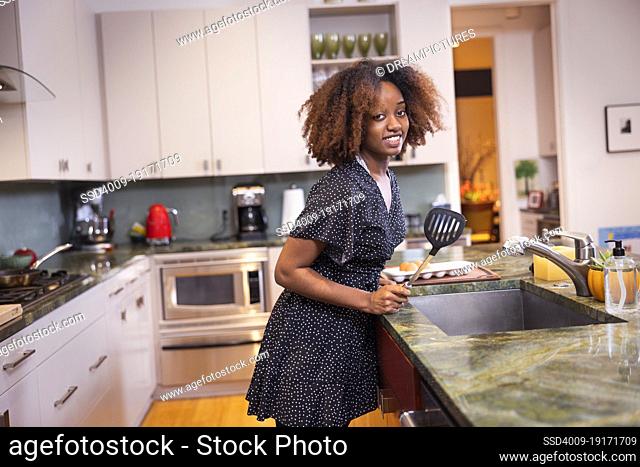 Young African American woman holding a spatula while cooking in a residential kitchen