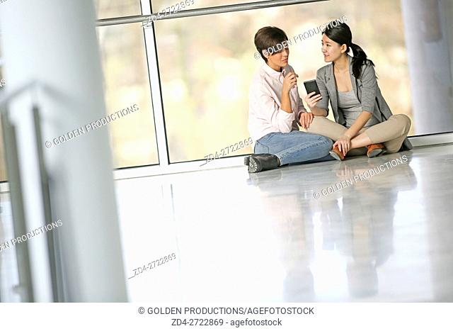 Two Businesswomen using smartphone while sitting