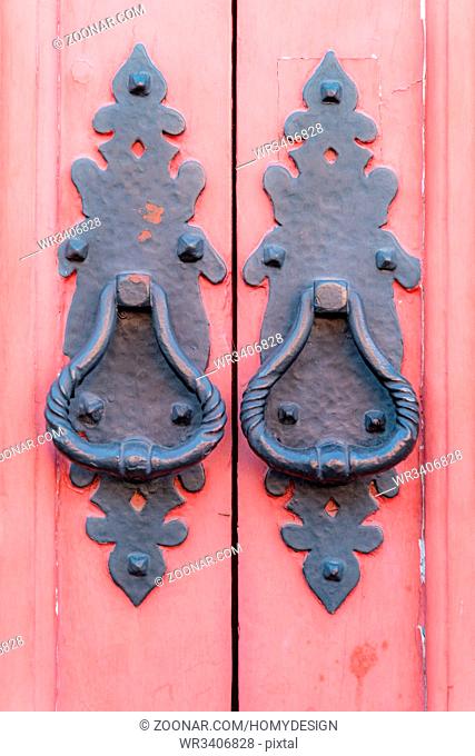 Vintage metallic door handles black on a wooden red painted wooden door background, concept of authentic objects, copy space, close-up