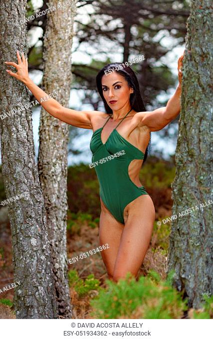 Fitness girl posing in the beach forest between .trees with a beautiful green swimsuit