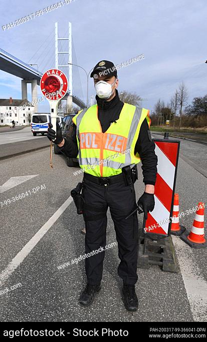 17 March 2020, Mecklenburg-Western Pomerania, Stralsund: With a holding trowel, a police officer regulates vehicle traffic in the direction of the island of...