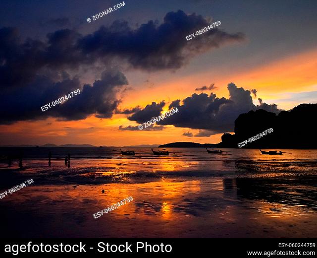 Beautiful sunset scene with dramatic sky over sea shore beach with traditional longtail boats in Thailand