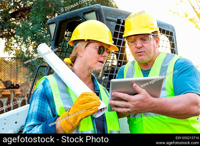Male and Female Workers With Technical Blueprints and Computer Tablet Talking at Construction Site