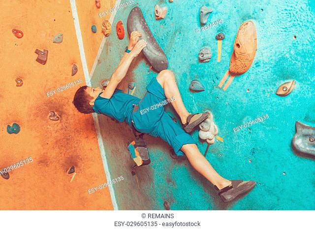 Free climber little boy climbing artificial boulder on practical wall in colorful gym