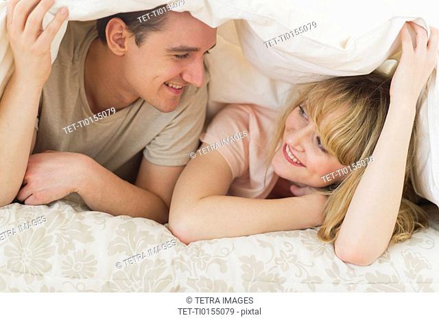 Couple lying on bed under duvet