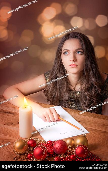 Beautiful young woman, with blue eyes, thinking what to write, at candlelight, surrounded by red and yellow globes and Christmas lights