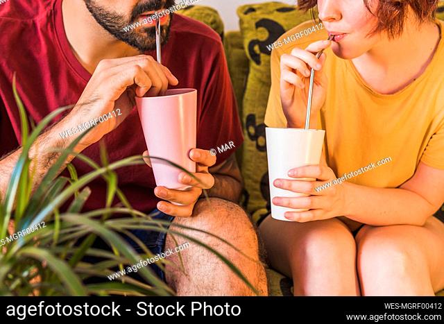 Couple holding bamboo glasses while drinking from metal straw at home