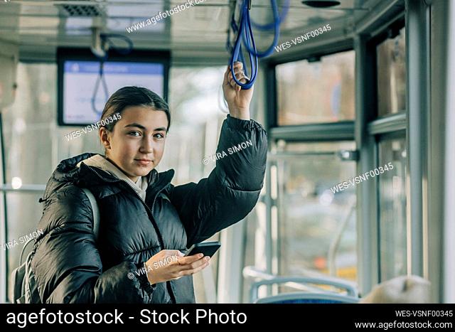 Smiling teenage girl standing with smart phone inside cable car