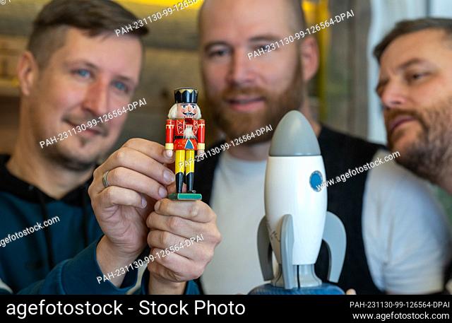 PRODUCTION - 27 November 2023, Saxony, Seiffen: Wooden toy maker Markus Füchtner (r-l), Tom Neubert and Mario Kaden look at the miniature nutcracker Wilhelm in...