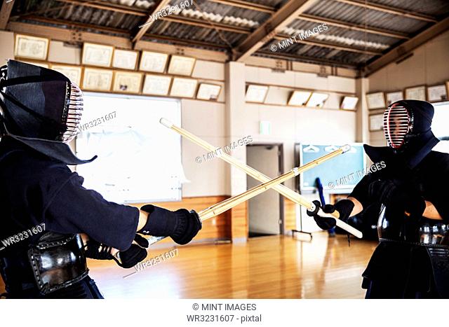 Two Japanese Kendo fighters wearing Kendo masks practicing with wood sword in gym