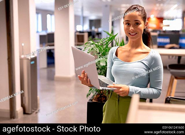 Portrait of smiling young female hispanic advisor holding laptop while working at modern workplace
