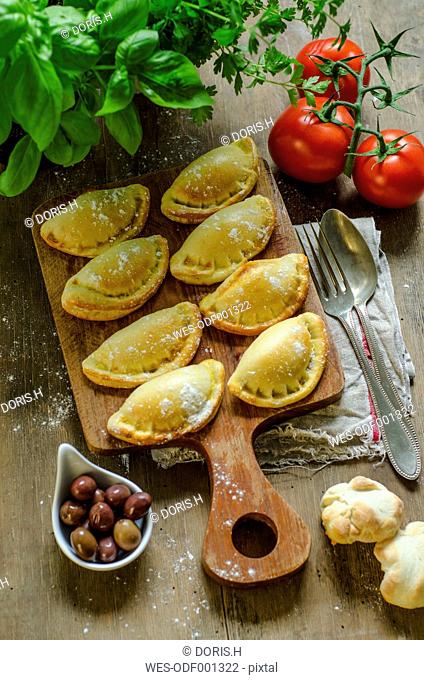 Stuffed pastry with black olives, tomatoes and basil on wooden board
